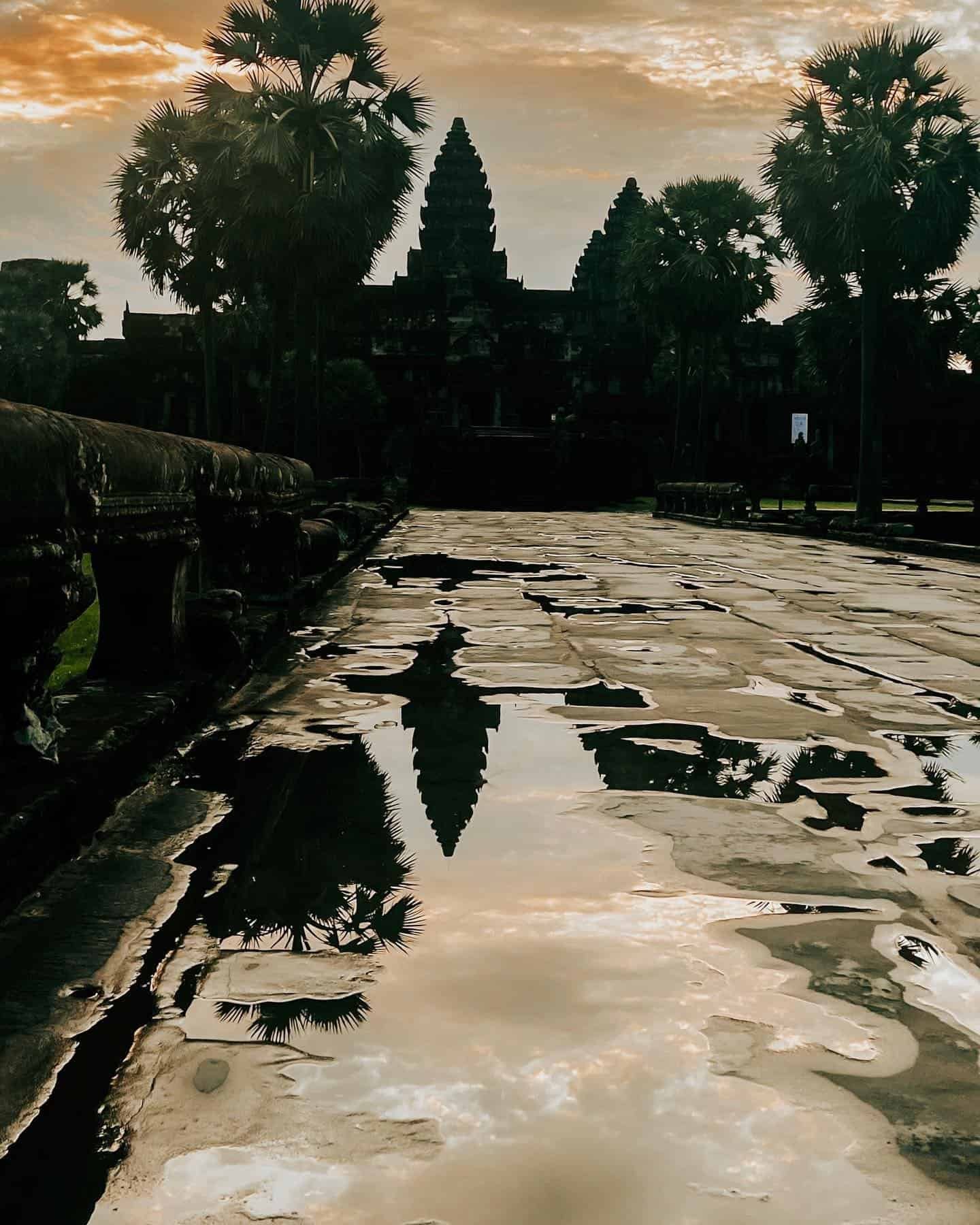 Angkor Wat at sunrise with the temple silhouetted against the morning sky and reflected in stone puddles
