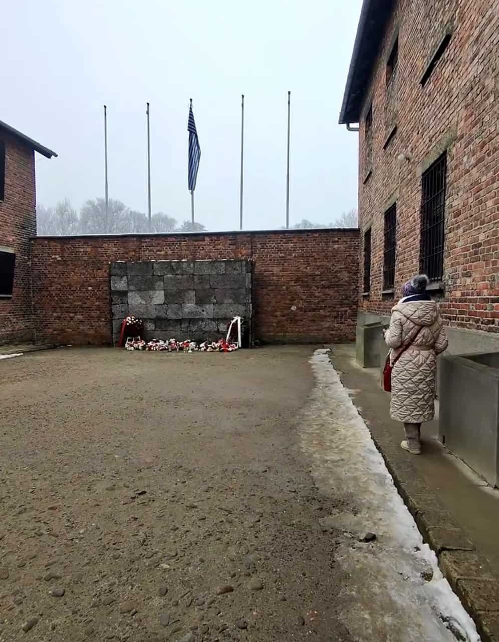 The Death Wall at Block 11 with wreaths and flowers left by visitors, our guide walking through the courtyard