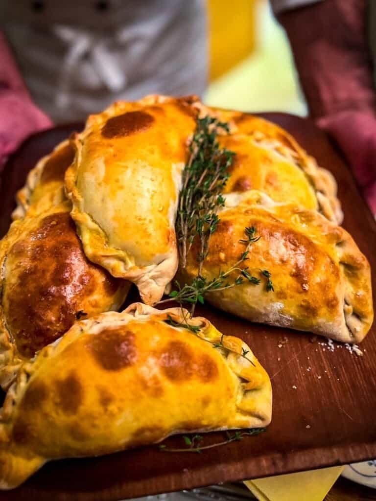 Freshly baked golden empanadas with thyme on a wooden serving board