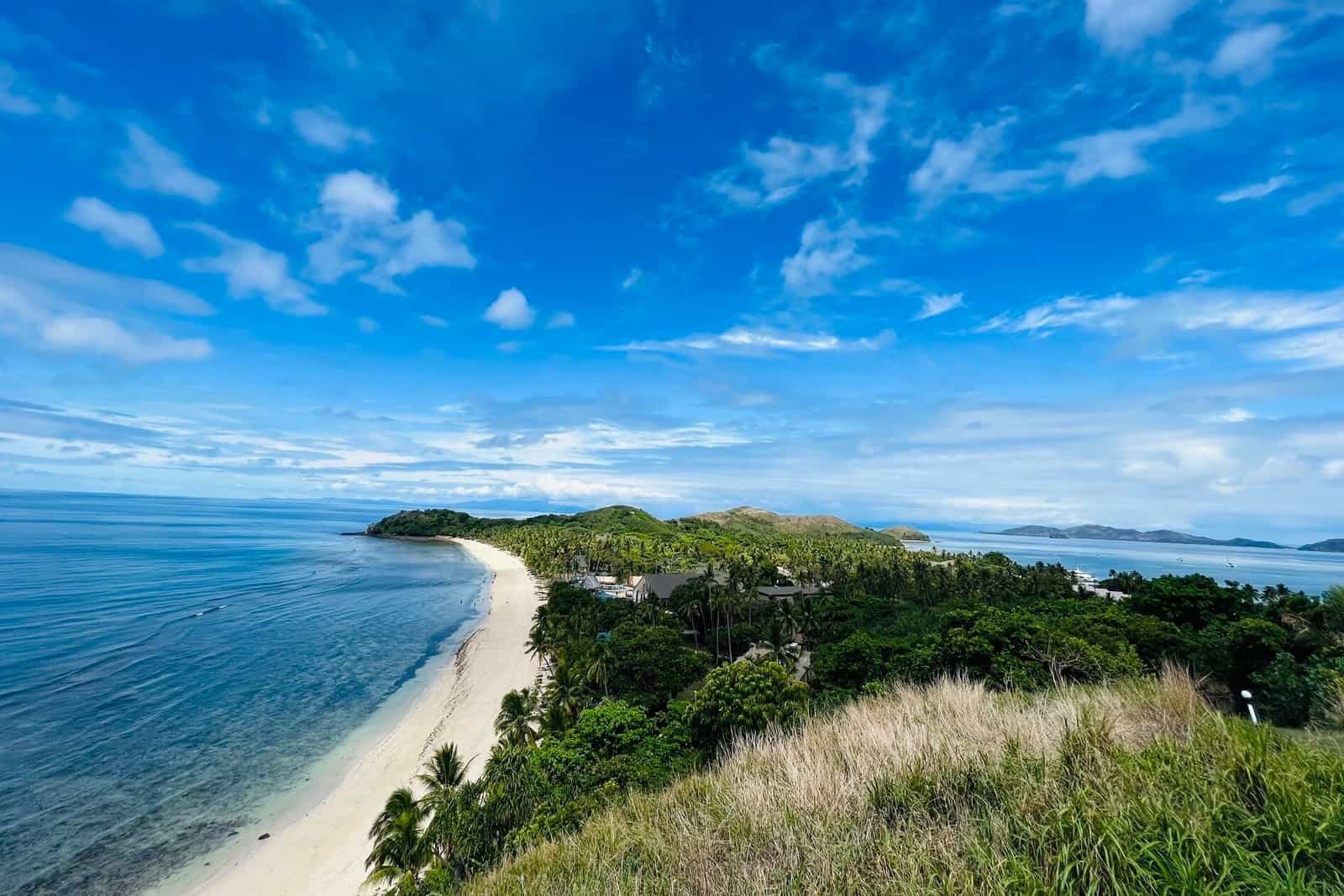 A white-sand beach curving along a lush tropical coastline in Hawaii under a bright blue sky
