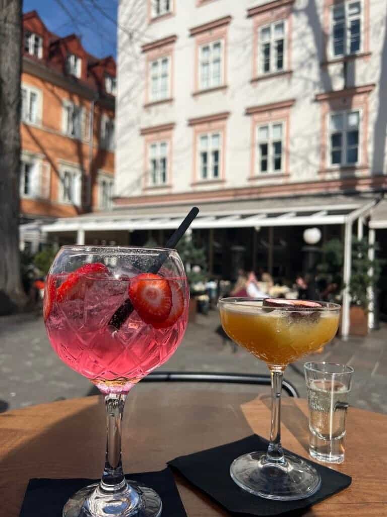 Two colorful cocktails on an outdoor cafe table with European architecture in the background