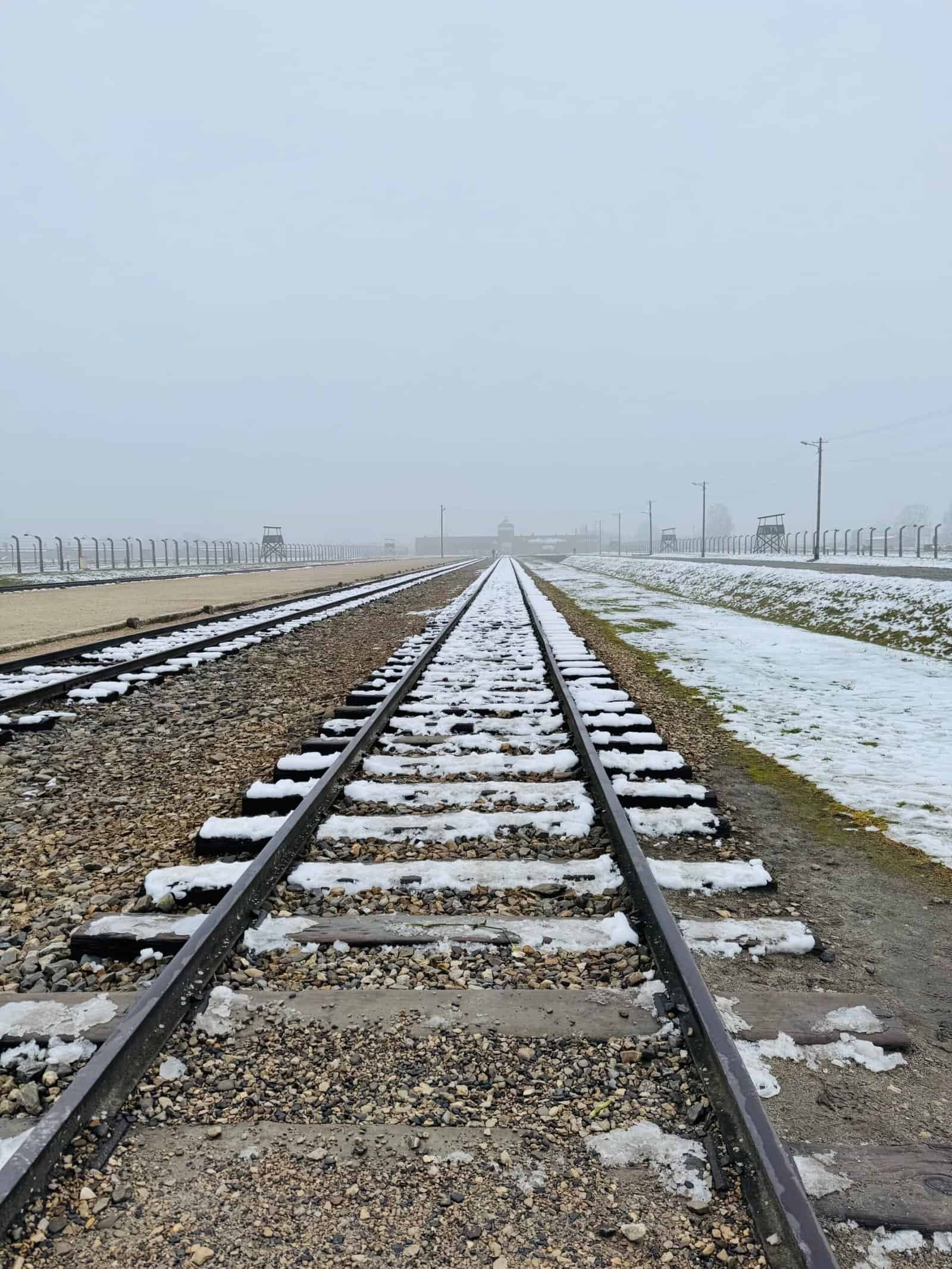 Empty railroad tracks at Birkenau leading into fog toward the gatehouse in winter