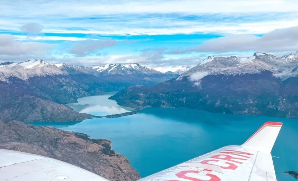 An aerial view from a small plane over snow-capped peaks and a turquoise glacial lake in Patagonia