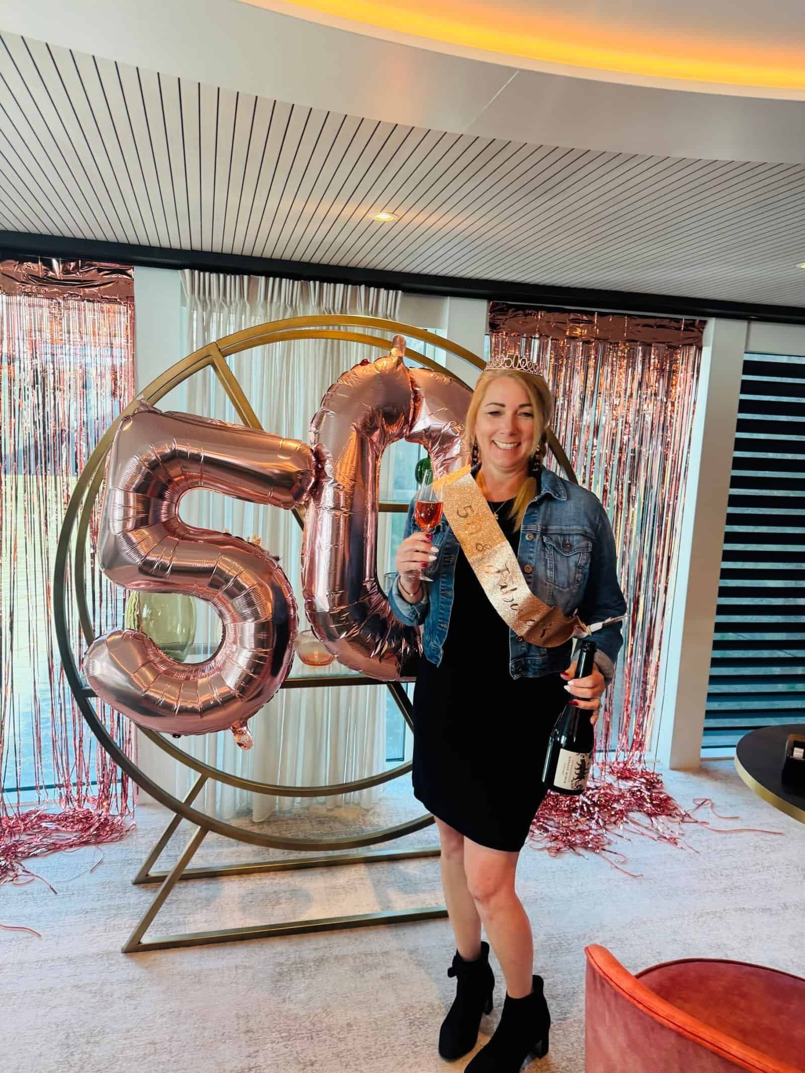 Charity Auger raising a glass beside rose gold fifty balloons aboard her Danube river cruise.
