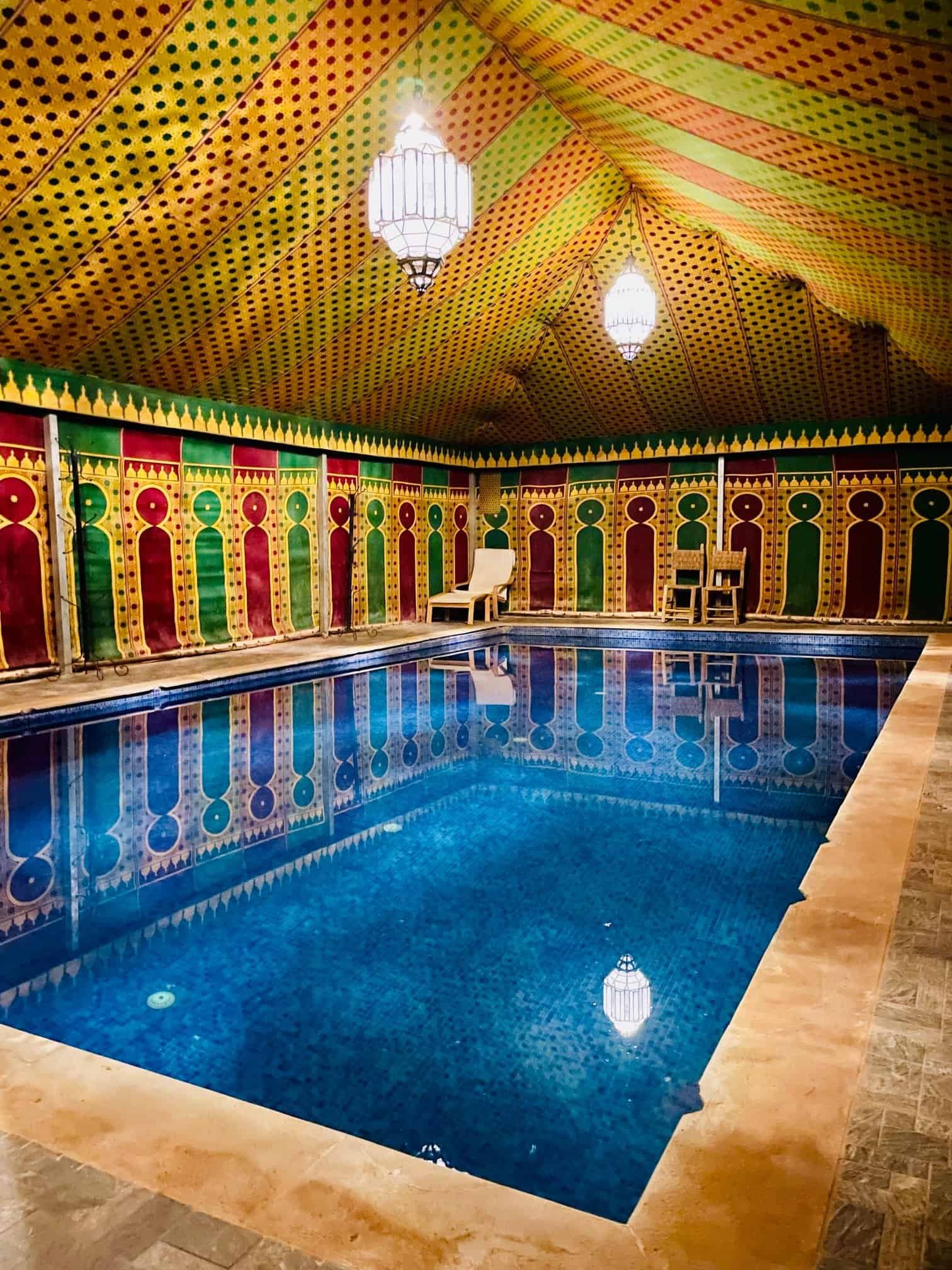 Indoor pool inside a traditional Moroccan painted tent in the Sahara desert, geometric patterns floor to ceiling, Moorish lanterns