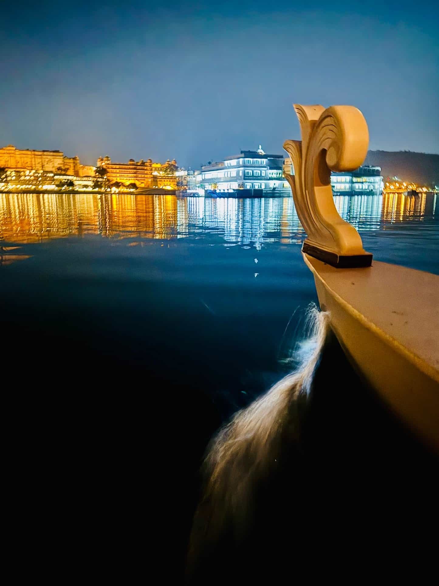 Nighttime arrival by boat at the Taj Lake Palace, palace glowing white across the water in Udaipur
