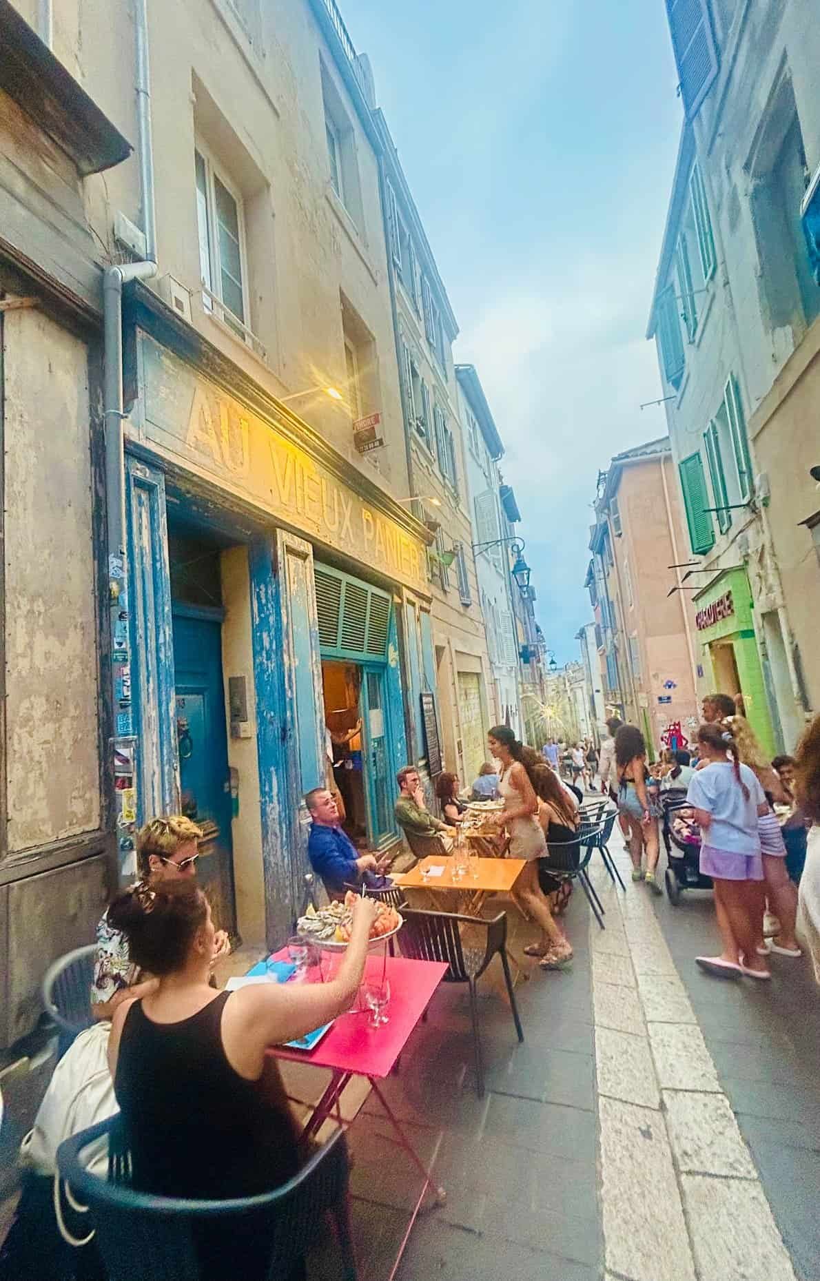 Diners at a small seafood spot along a narrow, painted lane in the Panier district of Marseille.