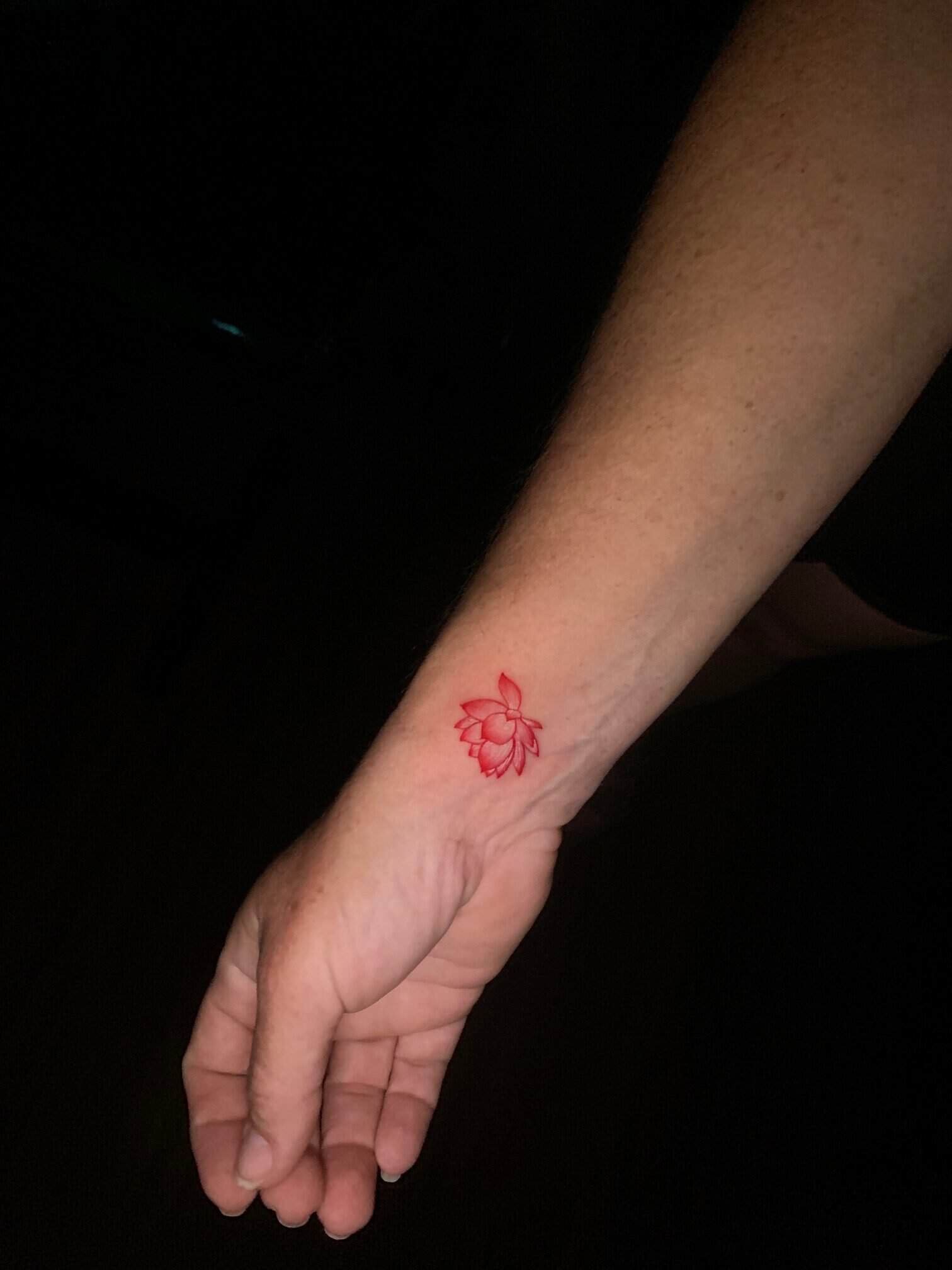 A small red lotus tattoo on the inside of Charity Auger's wrist, her arm held out against a dark background.