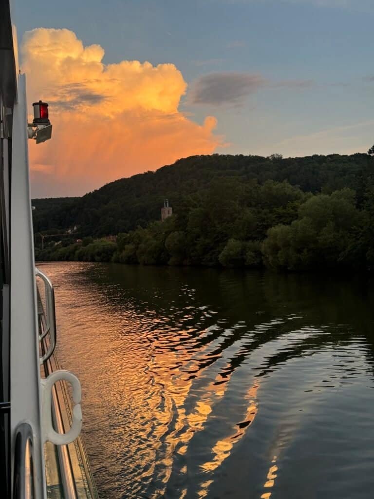 Sunset over a forested riverbank seen from the deck of a river cruise ship
